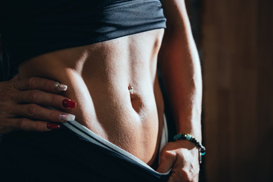detail of the body fitness of a girl, with a piercing in navel and nails painted