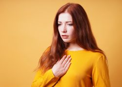 sad young woman with hand on chest feeling sick from heartache or heartburn