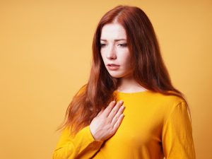 sad young woman with hand on chest feeling sick from heartache or heartburn